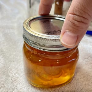 A person is using two finger to tighten the canning ring on a mason jar. This demonstrates the “finger tight” method.