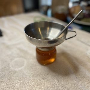A canning funnel sits on top of a mason jar filled with jam. A chopstick is inside the funnel