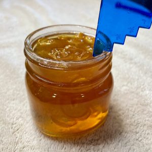 A small jar of jam is being measured with a canning headspace tool.