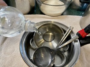 A small cooking pot filled with canning tools. Someone is pouring white vinegar into it.