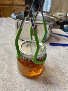A set of canning tongs is being used on a mason jar to lift it into the canner.