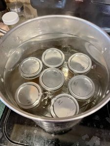 Seven filled mason jars are inside a large water bath canning pot of boiling water.